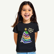 Child wearing a black t-shirt with a colorful Christmas tree design and text.