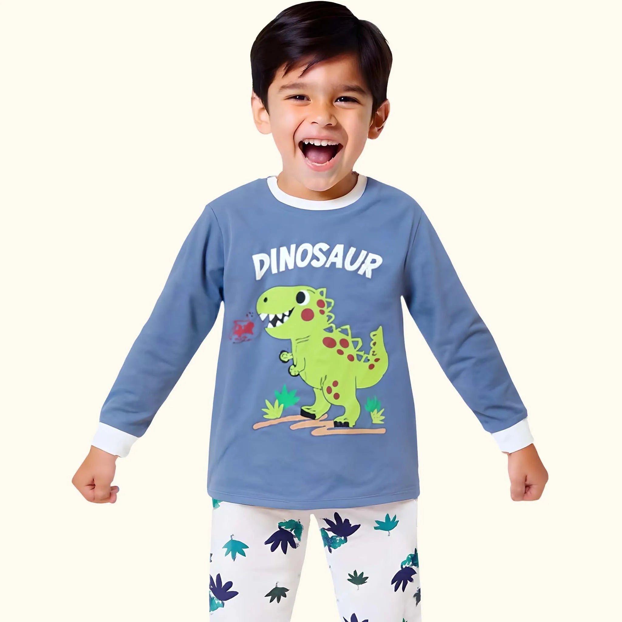 Child wearing a blue long-sleeve shirt with a dinosaur design and white pants with dinosaur patterns on a white background.