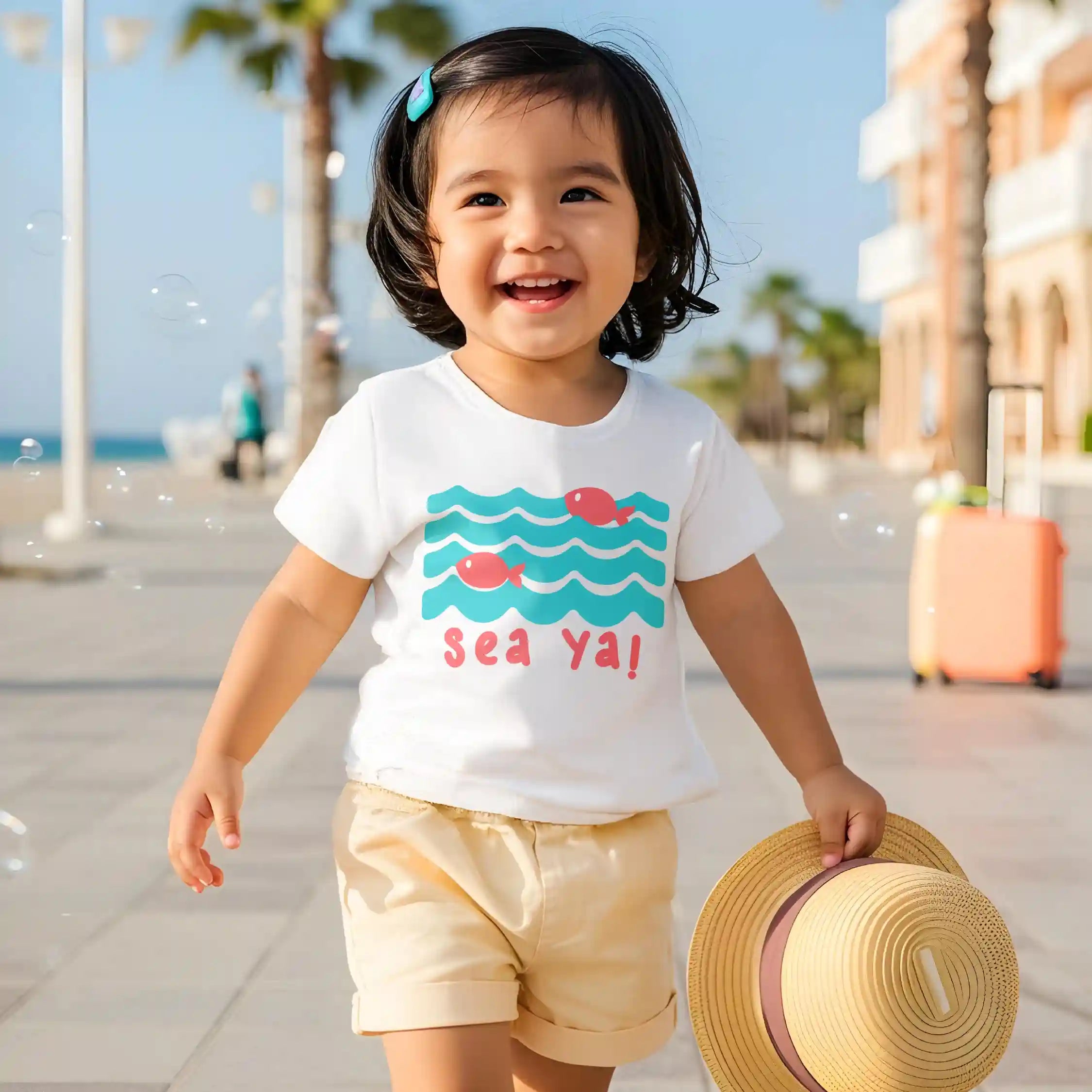 Child wearing a white t-shirt with a sea-themed design and shorts, holding a hat on a sunny day.