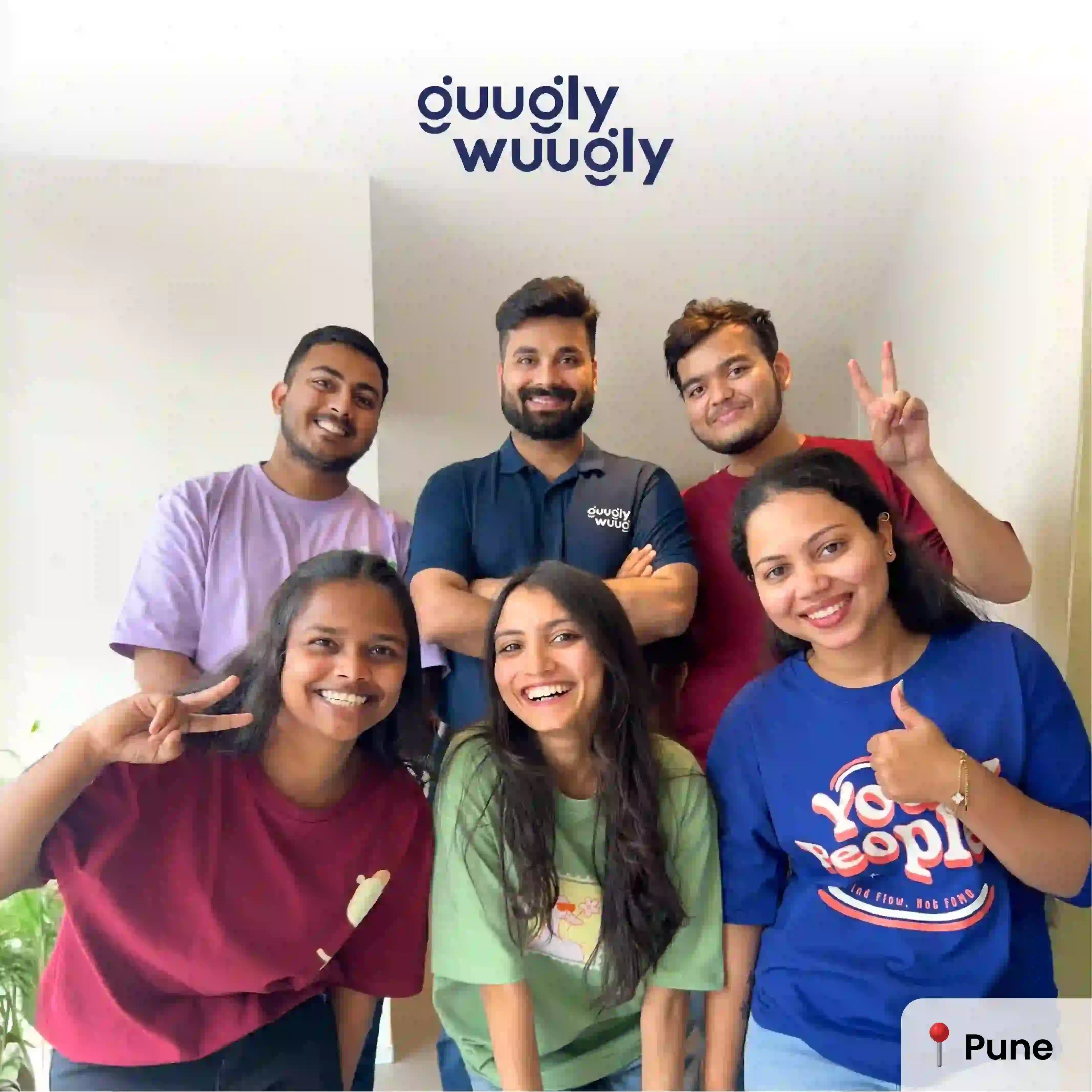 Group of six people posing together with 'guugly wuugly' branding in the background.