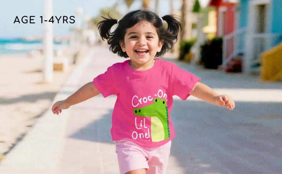 Child wearing a pink shirt with a green dinosaur design, running on a beach.